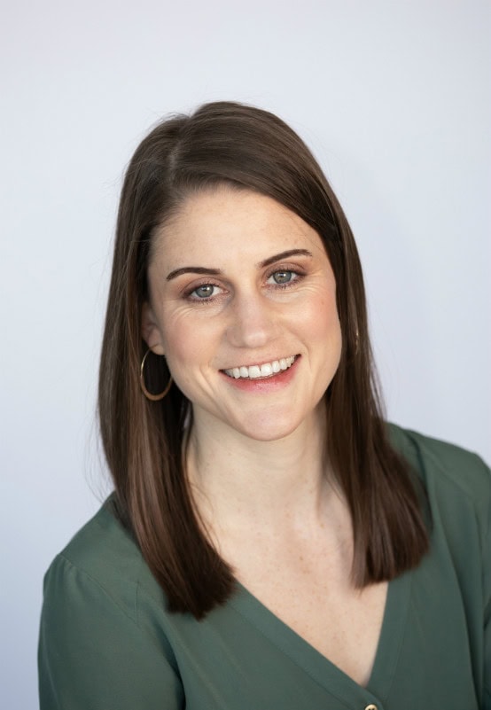 Smiling woman with brown hair and blue eyes wearing a green top and hoop earrings.