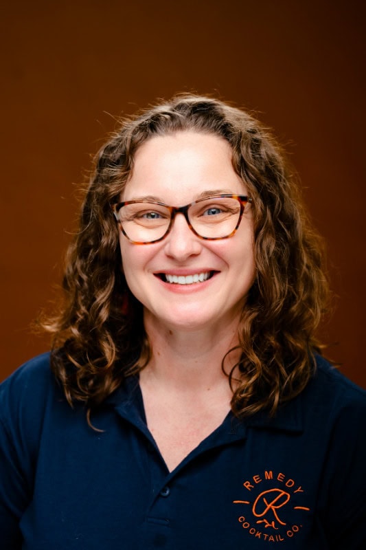 Smiling woman with curly hair and glasses wearing a navy polo shirt.