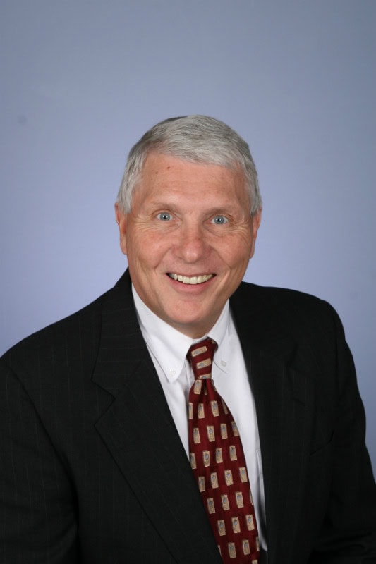 Smiling man in a suit with a patterned tie against a blue background.