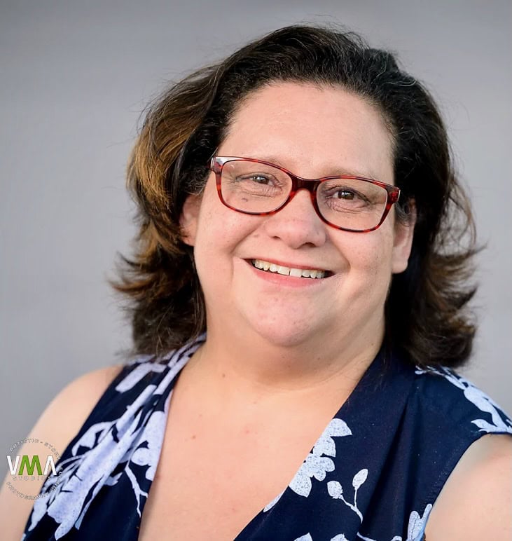 Woman with glasses smiling, wearing a blue and white floral top.