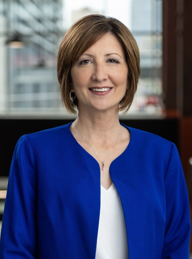 Woman with short brown hair in a blue blazer smiling indoors.