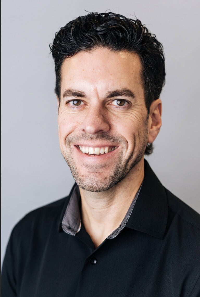 A smiling man with dark, curly hair wearing a black shirt.
