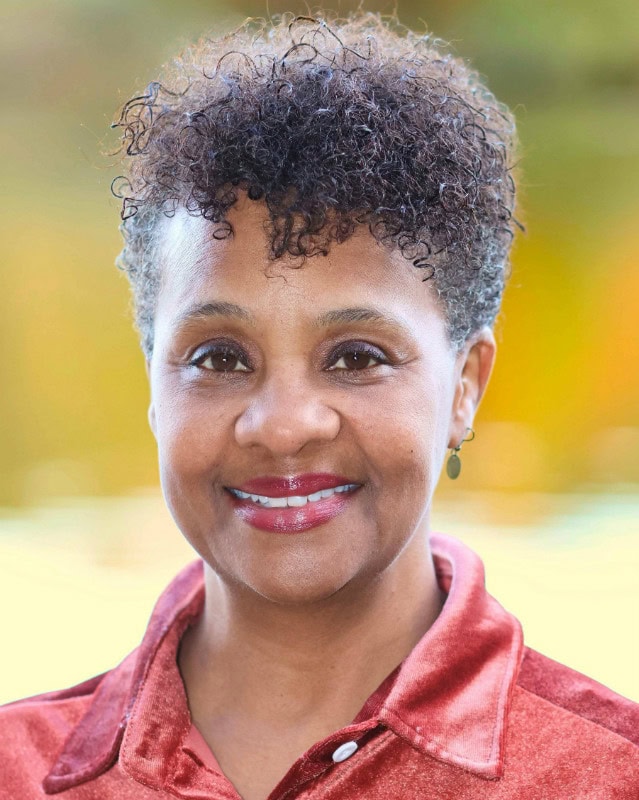 Close-up of a woman with short curly hair smiling outdoors.